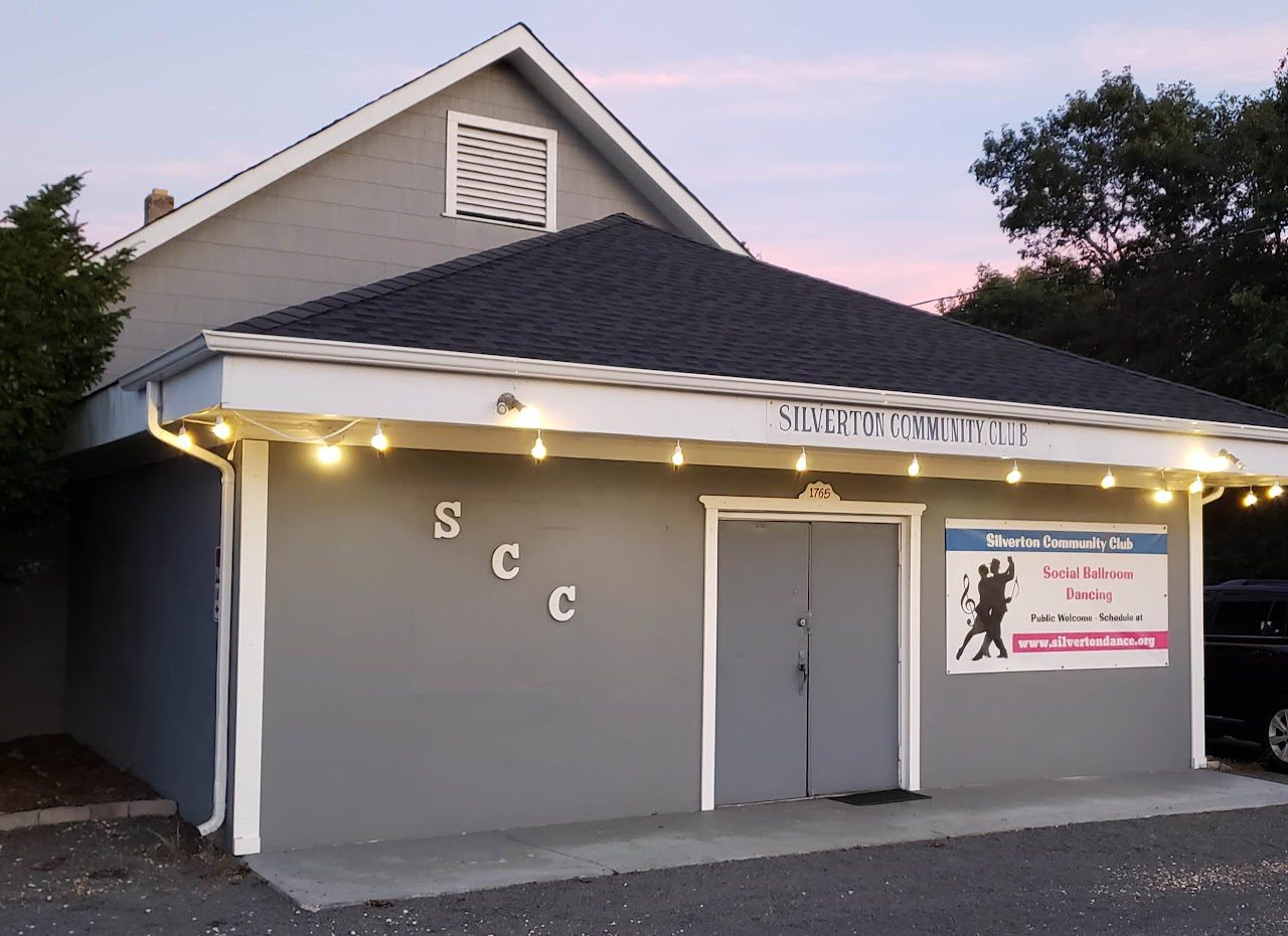 Gray building with lights hanging from awning with sign: Silverton Community Club