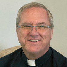 Man with gray hair and glasses wearing a clerical shirt