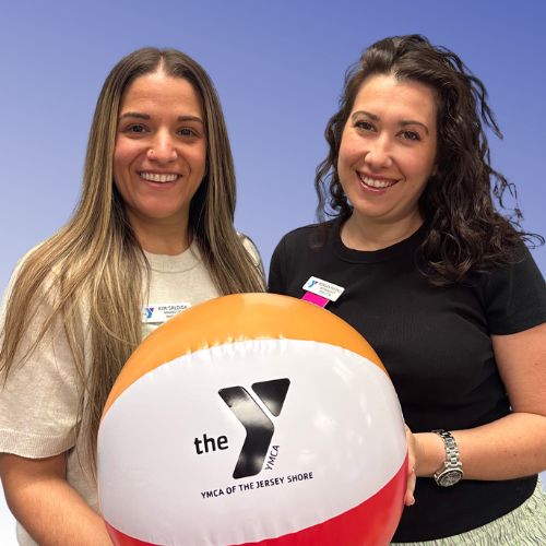 Two women holding a beach ball with the YMCA logo on it
