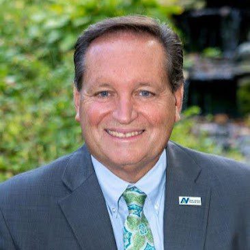 Man with short brown hair wearing a gray suit and a blue and green paisley printed tie