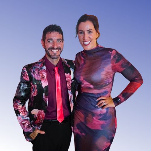 A man with dark hair and goatee wearing a colorful jacket next to a woman with dark hair wearing a purple and pink dress 